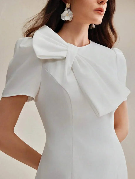 This elegant white dress features a structured silhouette with a dramatic bow at the neckline, perfect for making a.