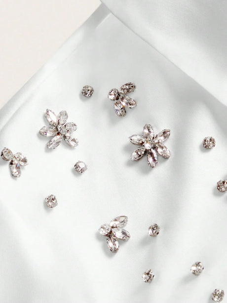 Delicate white satin fabric adorned with sparkling jewel embellishments in floral shapes creates a breathtakingly elegant.