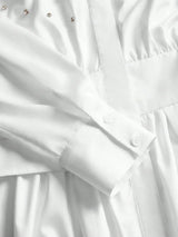 This elegant white dress features a sophisticated button-up design with delicate detailing along the bodice, complemented by.