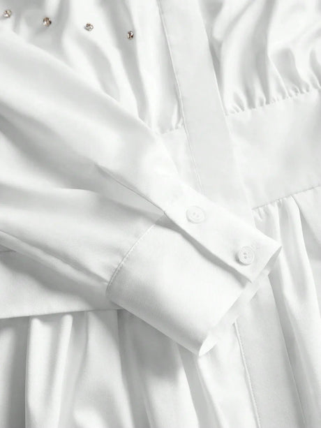This elegant white dress features a sophisticated button-up design with delicate detailing along the bodice, complemented by.