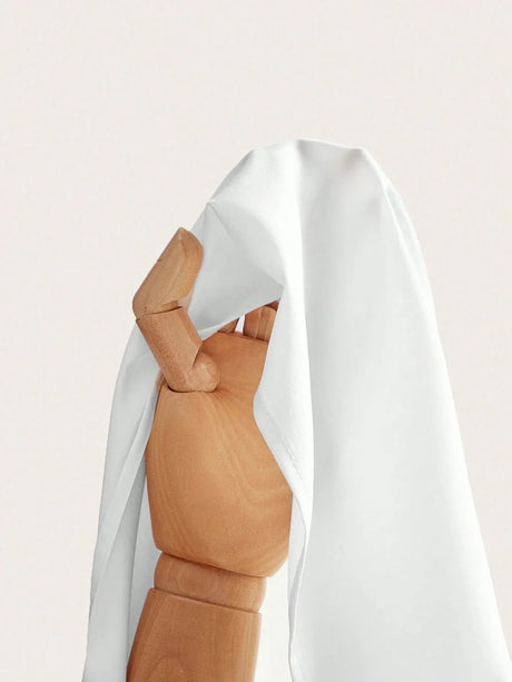 A flowing white dress drapes elegantly over a wooden mannequin, showcasing its soft fabric and relaxed fit. The lightweight.
