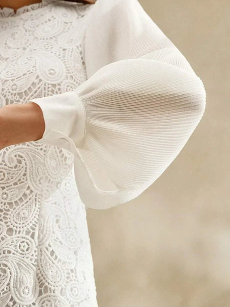 This elegant white dress features intricate lace detailing and soft pleated puff sleeves that create a romantic silhouette..
