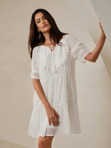 Light and airy, this white dress features delicate lace detailing along the puffed sleeves and a charming tie neckline,.