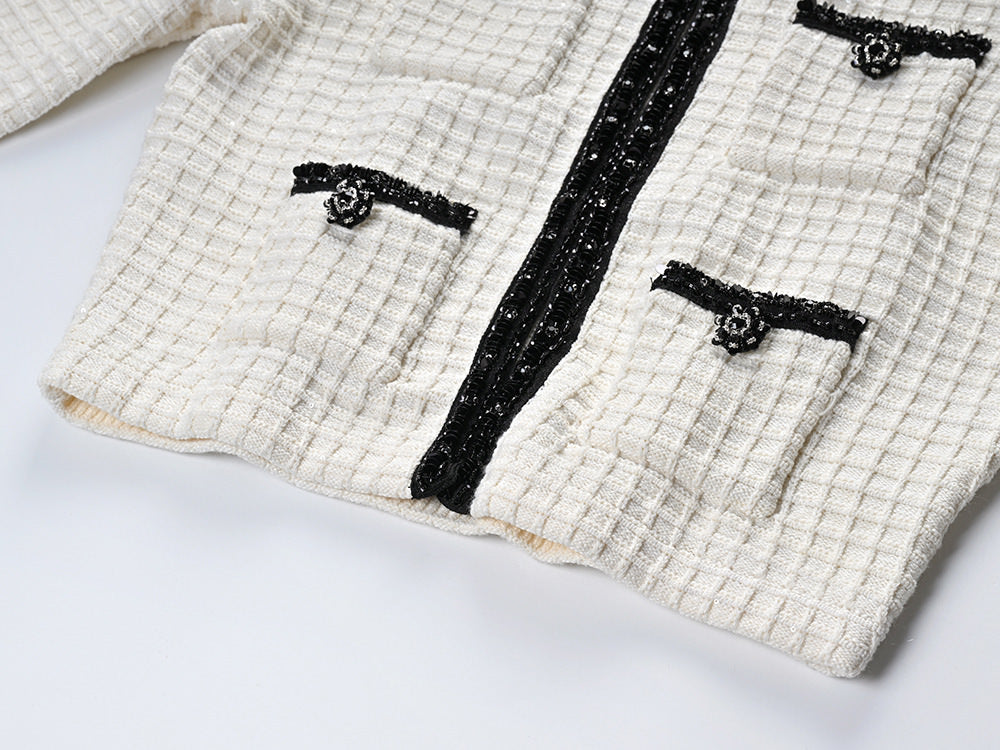 Textured white knitted jacket with black trim and decorative buttons paired with a ruffled hem skirt