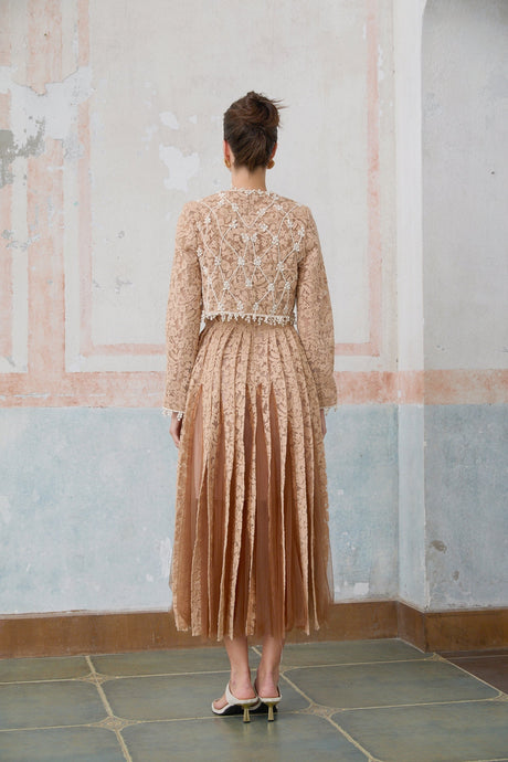 Woman wearing a beige crochet lace cardigan over a matching midi dress with delicate floral patterns standing in a neutral background