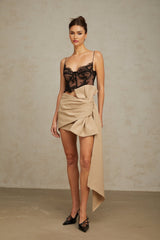 Woman wearing a beige mini skirt with ruched detailing and a decorative bow accent at the waist
