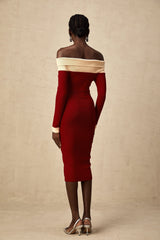 Woman wearing a beige offshoulder knit midi dress with long sleeves standing against a plain background