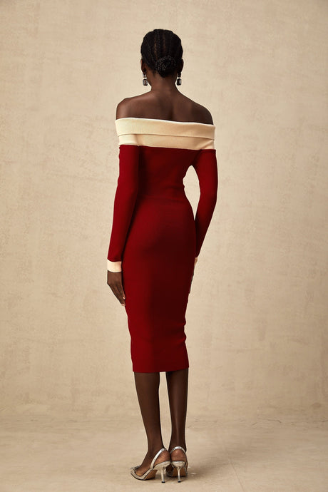 Woman wearing a beige offshoulder knit midi dress with long sleeves standing against a plain background