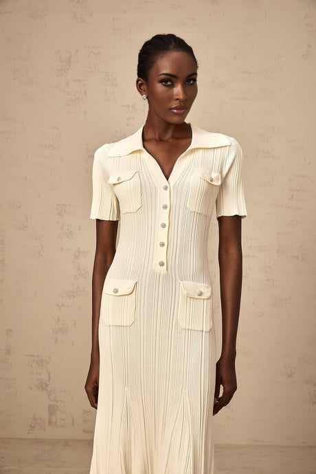 Woman wearing a beige ribbedknit midi dress with long sleeves and a slim fit silhouette standing against a plain background