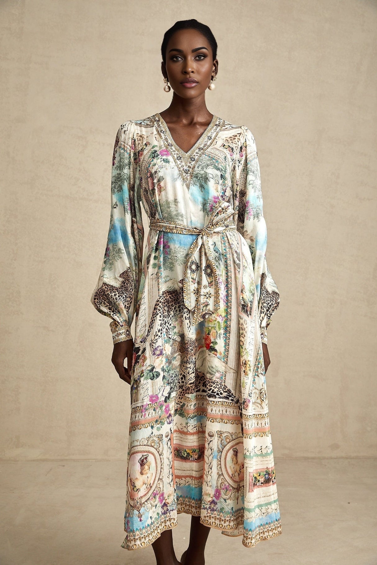Woman wearing a belted midi dress with Vneck in flowing fabric standing against plain background