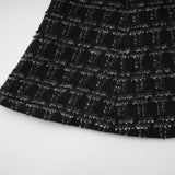 Woman wearing a black checked tweed matching set consisting of a sleeveless vest top and skirt with a plaid pattern