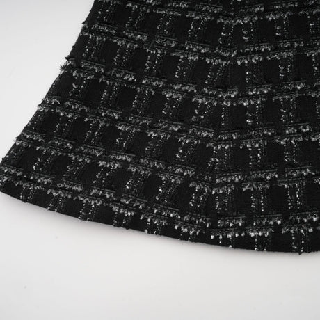 Woman wearing a black checked tweed matching set consisting of a sleeveless vest top and skirt with a plaid pattern