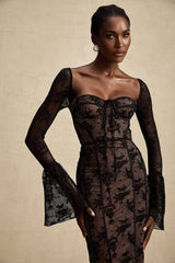 Woman wearing a black flared lace maxi dress with long sleeves and a floorlength skirt