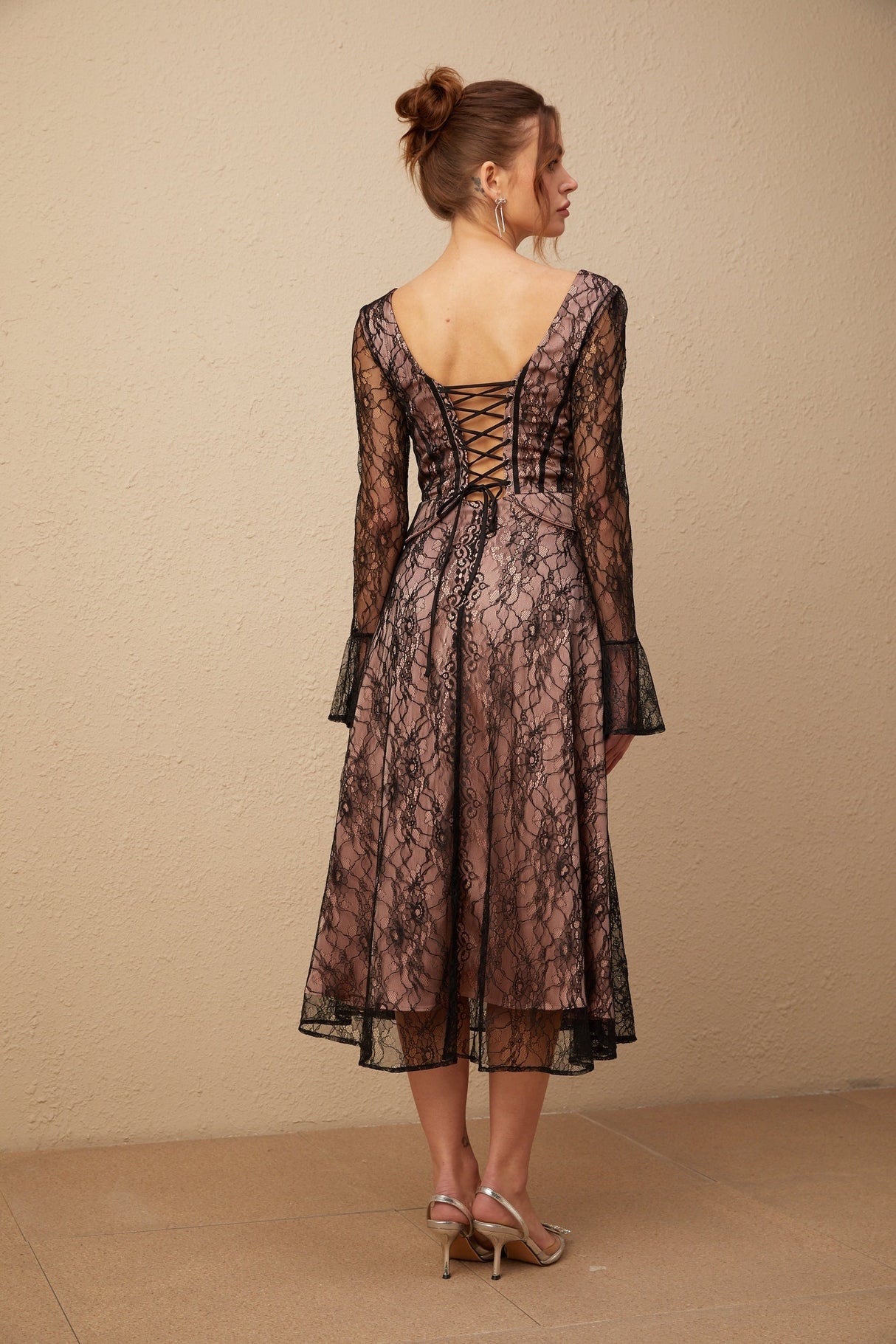Woman wearing a black lace midi dress with flared skirt and short sleeves standing against a plain background