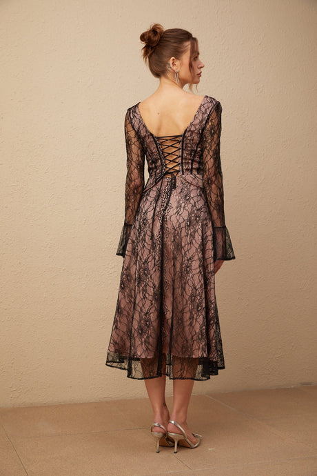 Woman wearing a black lace midi dress with flared skirt and short sleeves standing against a plain background