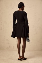 Woman wearing a black long sleeve mini dress with a flared skirt standing against a plain background