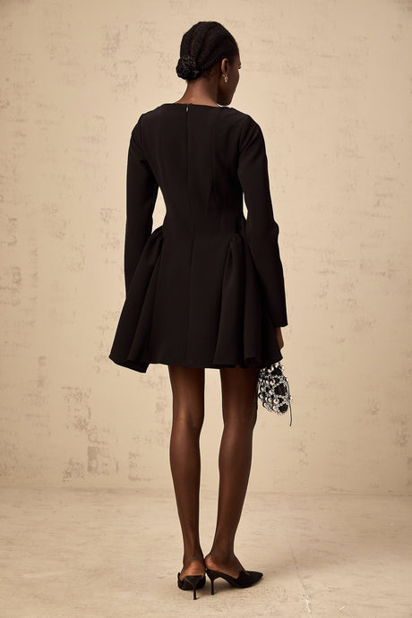 Woman wearing a black long sleeve mini dress with a flared skirt standing against a plain background