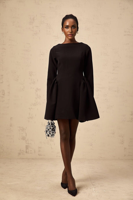 Woman wearing a black long sleeve mini dress with flared skirt standing against plain background