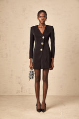 Woman wearing a black mini dress with lion head embellishments on the blazer style top