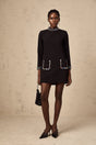 Woman wearing a black mini dress with long sleeves and crystal embellishments