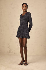 Woman wearing a black mini dress with sequin embellishments and knit texture form fitting silhouette short hemline