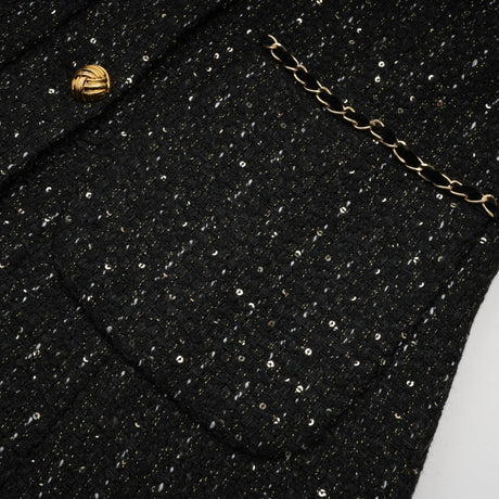 Woman wearing a black mini dress with sequin panels and tweed fabric short sleeves and form fitting silhouette