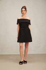 Woman wearing a black offshoulder mini dress with a belt cinching the waist standing against a plain background