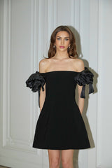 Woman wearing a black offshoulder mini dress with flower details on the bodice