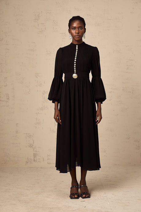 Woman wearing a black pleated midi dress with button front detail standing in a neutral pose