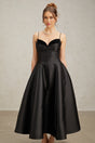 Woman wearing a black pleated midi dress with flared skirt and fitted waist standing against plain background