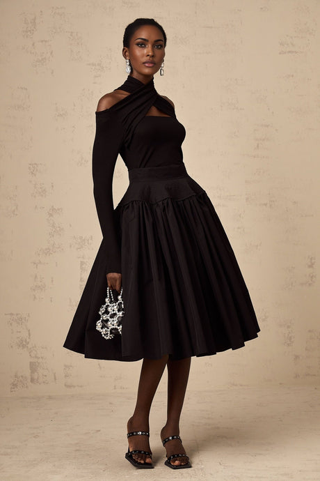 Woman wearing a black pleated midi skirt with flared silhouette standing against a plain background