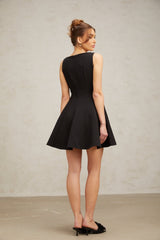 Woman wearing a black sleeveless mini dress with a flared skirt standing against a plain background