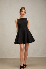 Woman wearing a black sleeveless mini dress with a flared skirt standing against a plain background