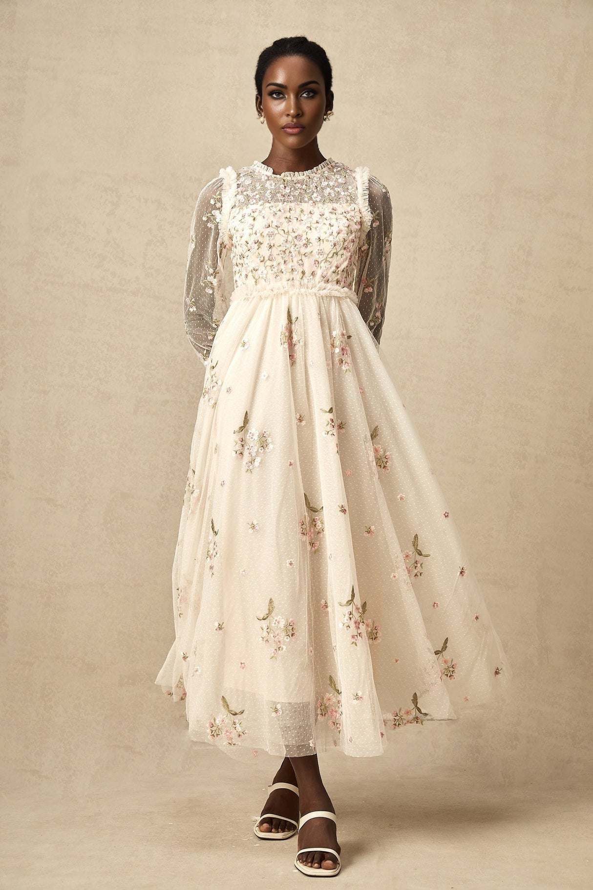 Woman wearing a black tulle midi dress with colorful floral embroidery featuring long sleeves and a high neckline