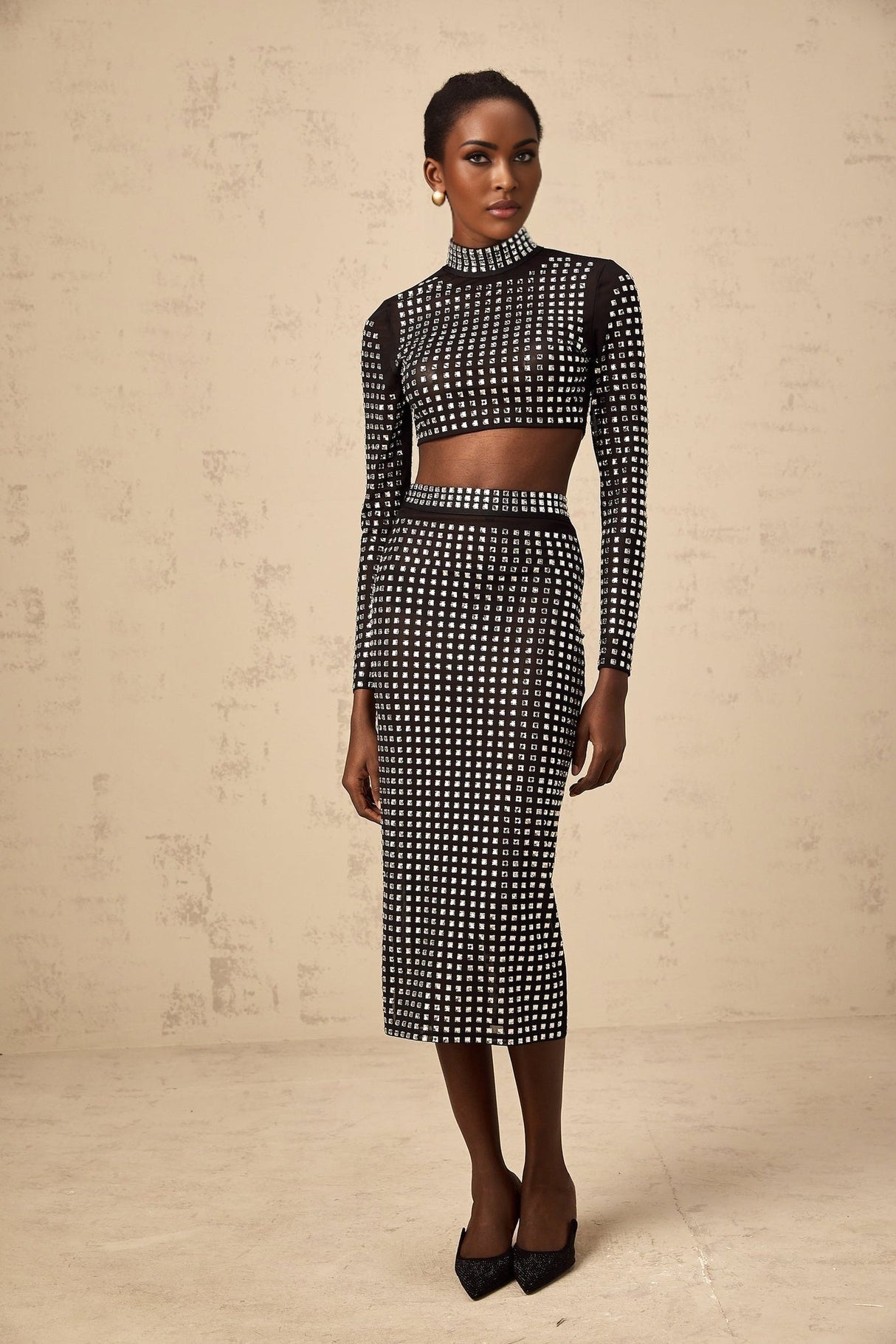 Woman wearing a black twopiece outfit consisting of a mesh top and skirt adorned with rhinestone embellishments