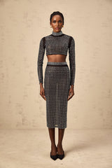 Woman wearing a black twopiece outfit consisting of a rhinestoneembellished mesh top and matching skirt