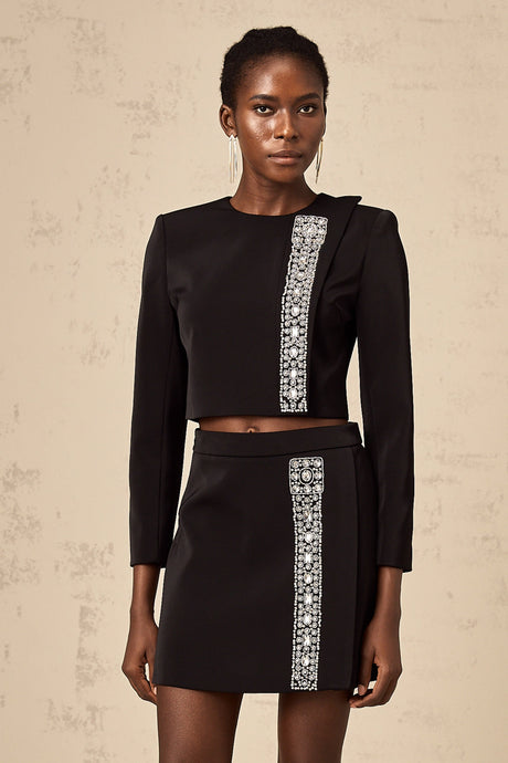 Woman wearing a black twopiece outfit consisting of a top and skirt adorned with crystal embellishments