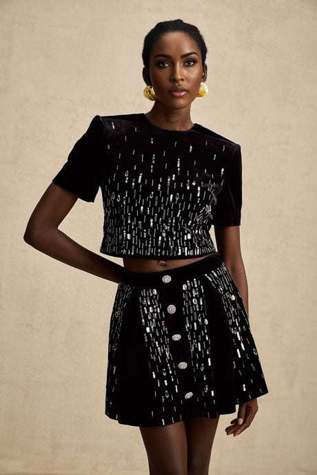 Woman wearing a black velvet matching set consisting of an embellished top and skirt named Isabeau
