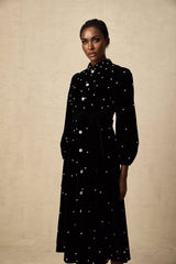 Woman wearing a black velvet midi dress with embellishments standing in a neutral background
