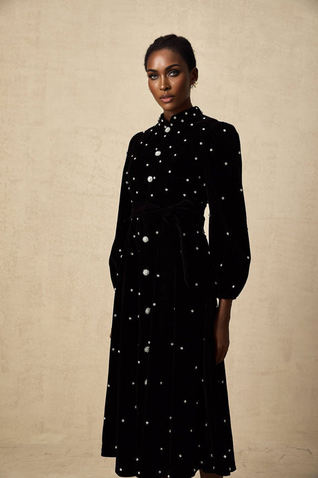 Woman wearing a black velvet midi dress with embellishments standing in a neutral background