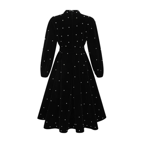 Woman wearing a black velvet midi dress with embellishments standing in a neutral background