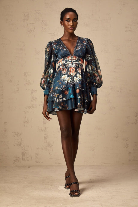 Woman wearing a blue mini dress with graphic print design and embellishments standing against a plain background