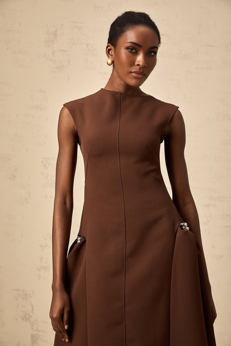 Woman wearing a brown asymmetric midi dress with flowing fabric and uneven hemline