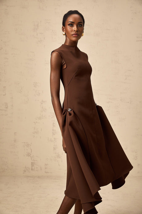 Woman wearing a brown asymmetric midi dress with flowing fabric and uneven hemline