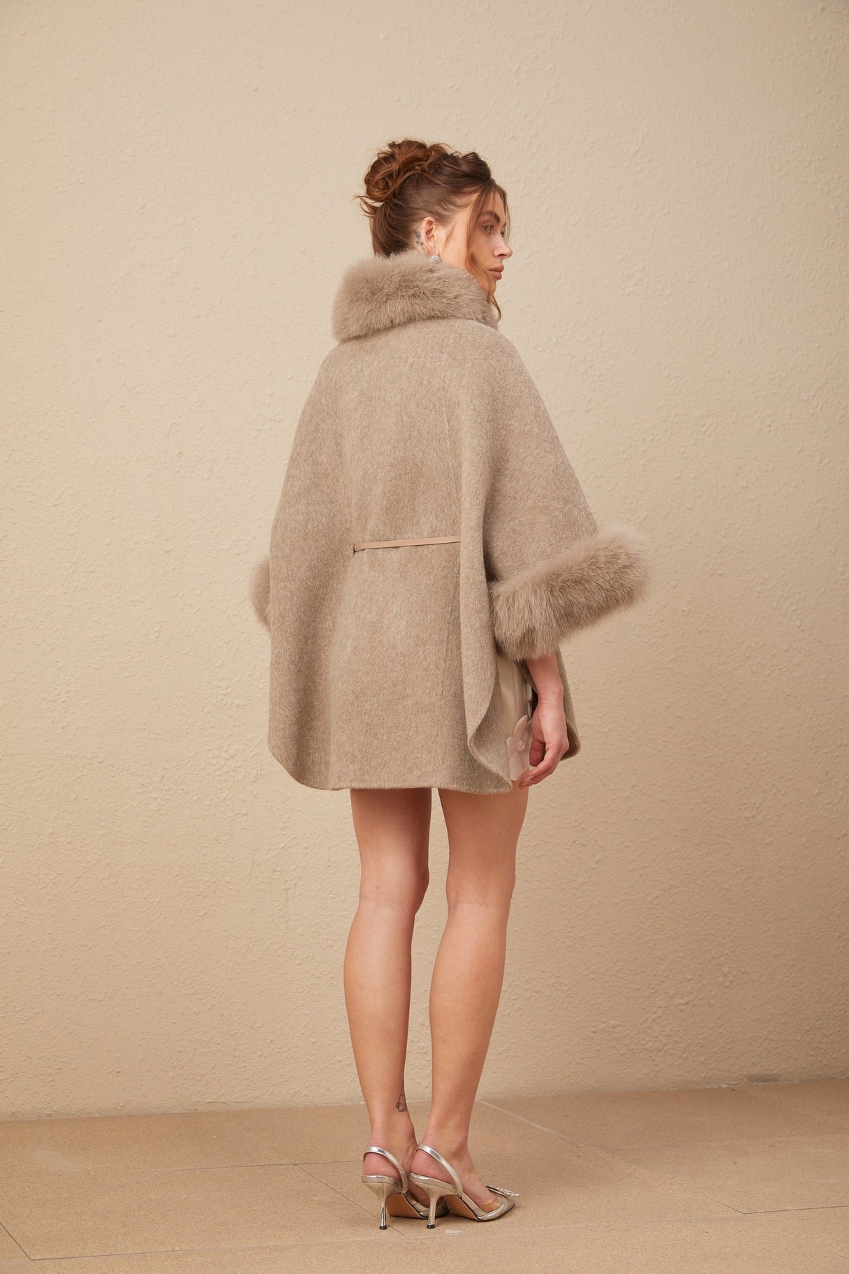 Woman wearing a brown wool cape coat with fur trim and belt fastened at the waist