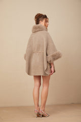Woman wearing a brown wool cape coat with fur trim and belt fastened at the waist