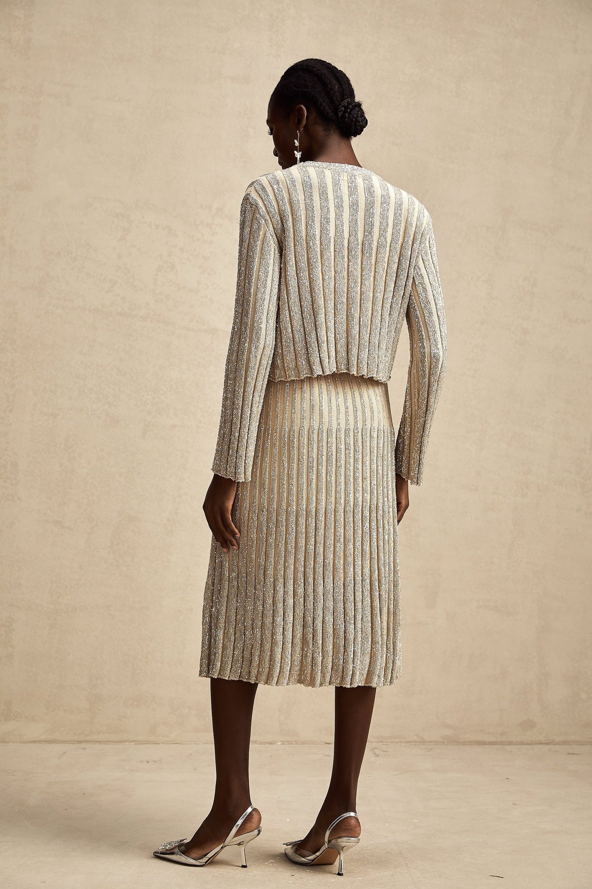 Woman wearing a champagne colored knit top and matching skirt with vertical stripes standing in a relaxed pose