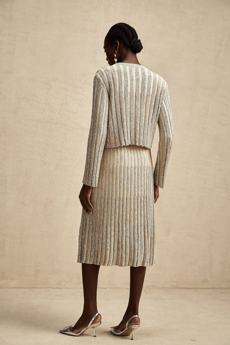 Woman wearing a champagne colored knit top and matching skirt with vertical stripes standing in a relaxed pose
