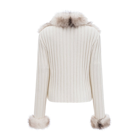 Woman wearing a cozy faux fur jacket with ribbed knit texture in a neutral color standing against a plain background