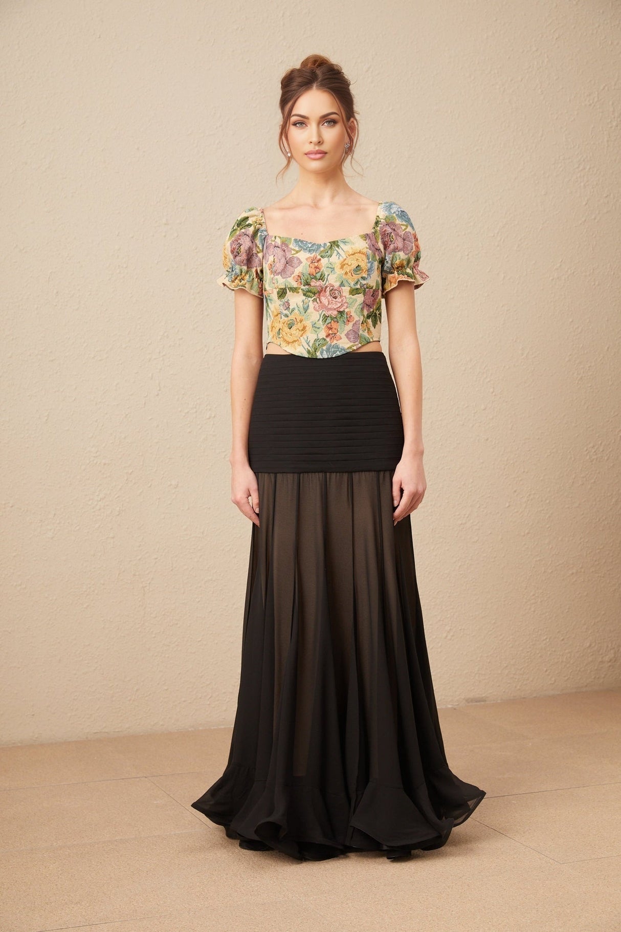 Woman wearing a cropped floral print top with short sleeves and a jacquard pattern in pastel colors against a plain background
